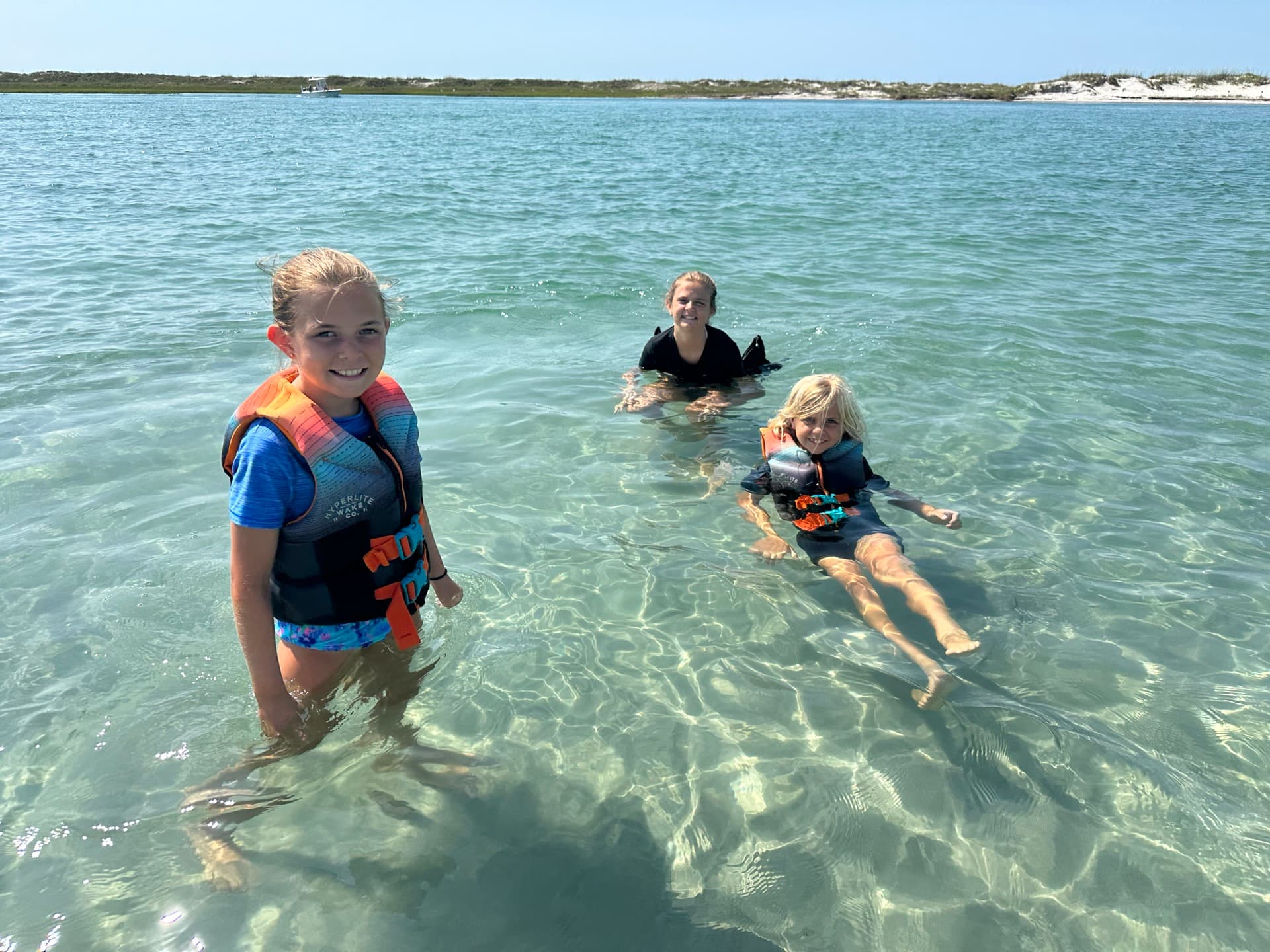 Three kids in life jackets swimming in clear, calm sound water at a Topsail sandbar